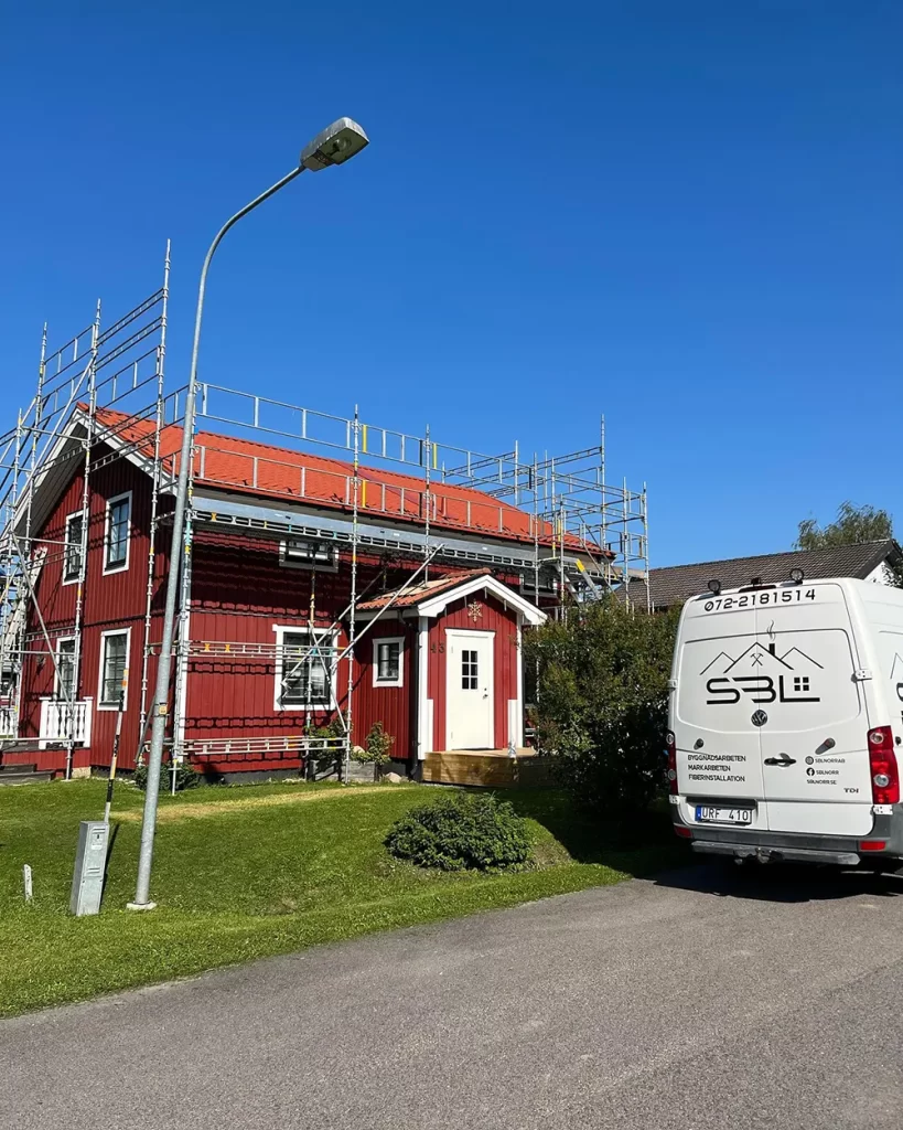 Ett rött hus där byggföretag SBL Norr AB uför takbyte. Himlen i bakgrunden är blå och en grön gräsmatta är framför huset. Dessutom står det en vit firmabil till vänster om bostaden.